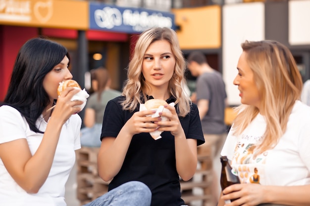 Pretty young women eating hamburger outdoor on the street.