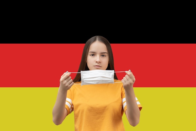 Prevention of coronavirus in Germany Young girl puts on an antibacterial medical mask on a flag background