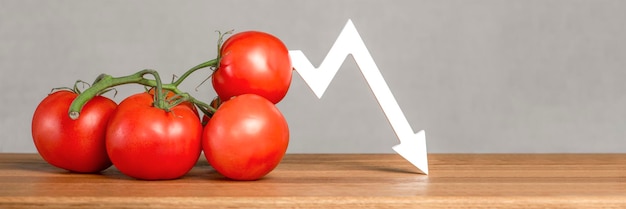 The price of tomatoes and vegetables Bad vegetable harvest Fresh red ripe tomatoes with twigs on the table Graph chart points down