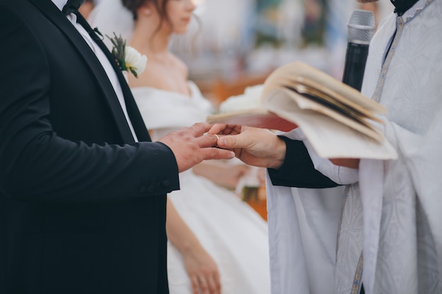 Priest is putting ring on groom's finger during orthodox wedding ceremony