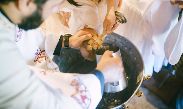 Priest washes the baby head from a jug during baptism over a basin