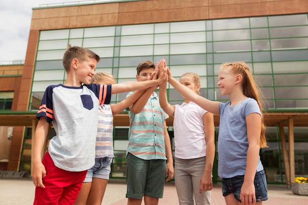 primary education, friendship, childhood and people concept - group of children or students making high five at school yard