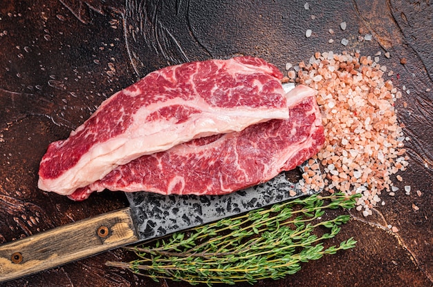 Prime Black Angus beef steaks  Raw Striploin or New York on a butchery meat cleaver. Dark background. Top view.