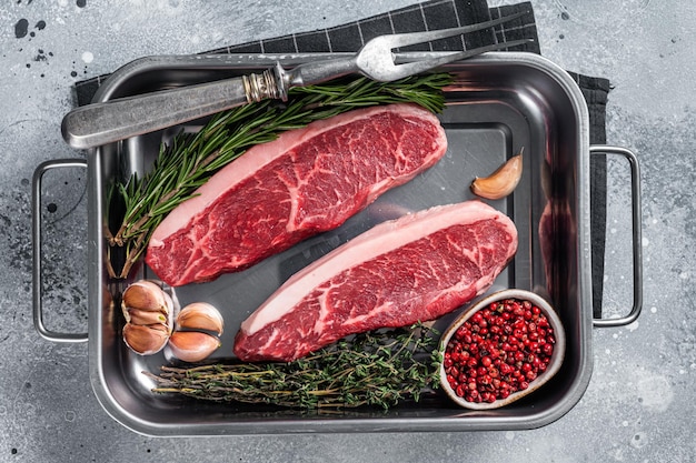 Prime Raw top sirloin beef or cap rump steak in tray with herbs Gray background Top view