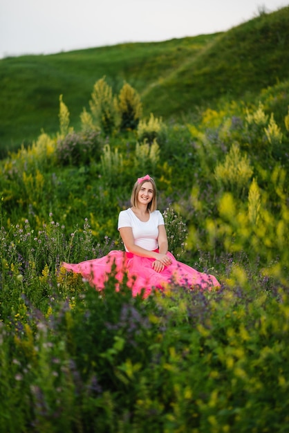 Princess in a summer pink dress sits on the green grass The girl in a flower field in a country