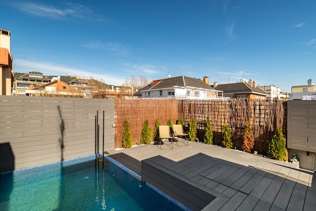 Private terrace on the roof of a house with swimming pool sunbeds and wooden fence on sunny day in b...