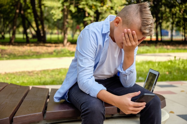 Problems of modern children. Young guy in the park with the phone upset