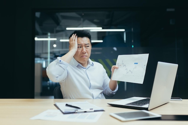 Problems with documents at work serious young asian businessman broker shows papers graphs to camera