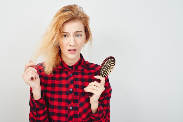 Problems with the hair. Girl with hairbrush on white background in the red shirt