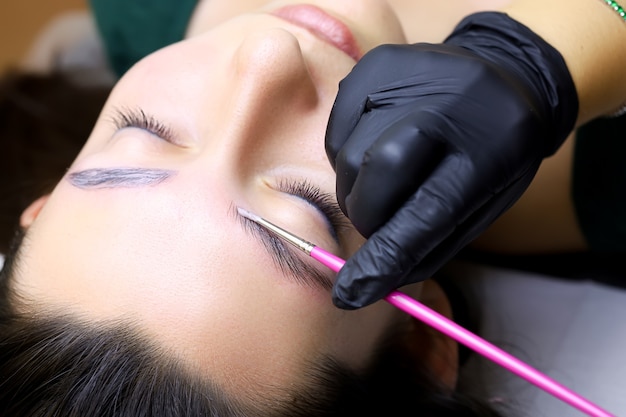 The procedure for long-term eyebrow styling is close-up, the master applies the composition for lamination of eyebrows with a brush