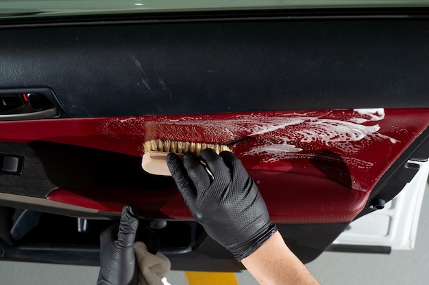 Process of detailing the car door panel with detergent Hand in a black glove cleaning a car door coating with a soapy brush Detailing procedure