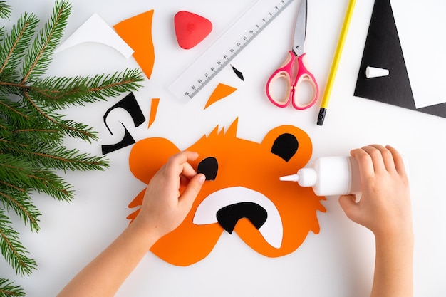 The process of making a childrens new year tiger mask with a child made of colored paper top view