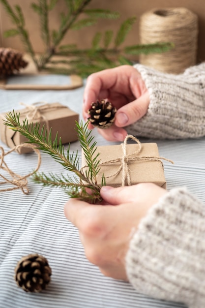 The process of packaging stylish modern gifts for Christmas and New year. Gift boxes made of Kraft paper, twine and Christmas tree branches. Christmas background, holiday atmosphere.