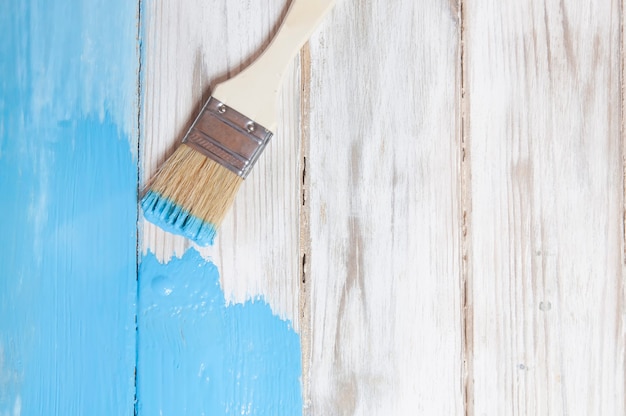 The process of painting with a wooden brush white old boards with blue paint top view