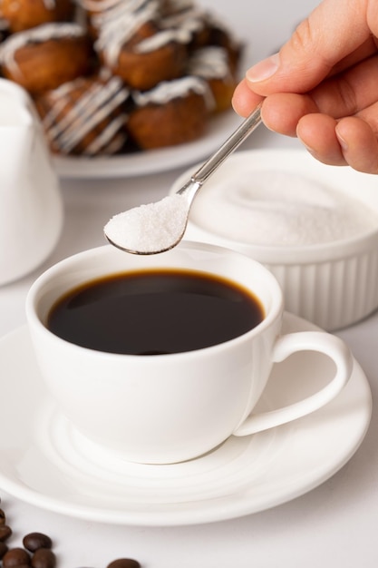 The process of pouring sugar from a spoon into a white cup of coffee