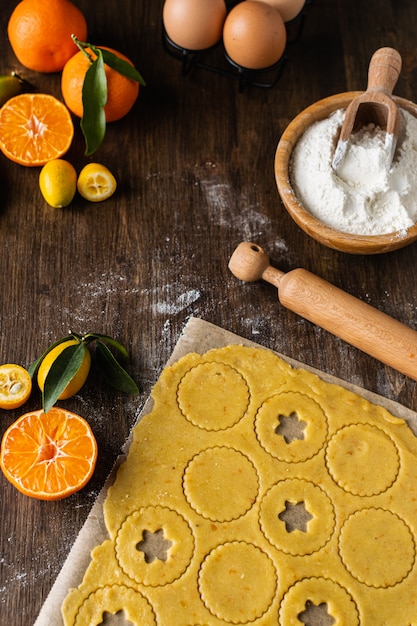 Process of preparation homemade traditional christmas linzer cookies, cookie dough, rolling pin, flour and tangerines on wooden table