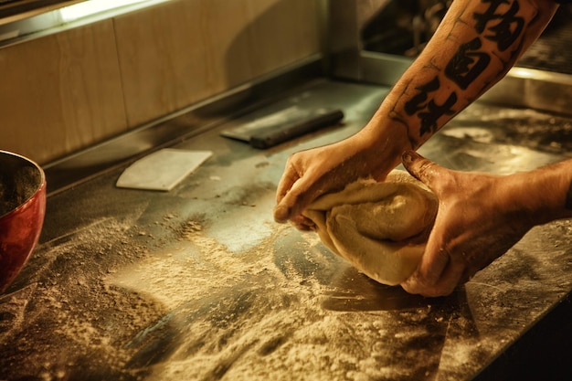 Process of preparation and making white homemade bread hands with tattoos of professional male baker making dough on table with flour concept of culinary and gastronomy