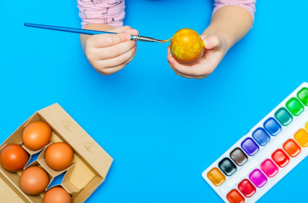 Photo the process of preparing for easter, the child paints easter eggs with a brush before the holiday. multi-colored paints. copy space.