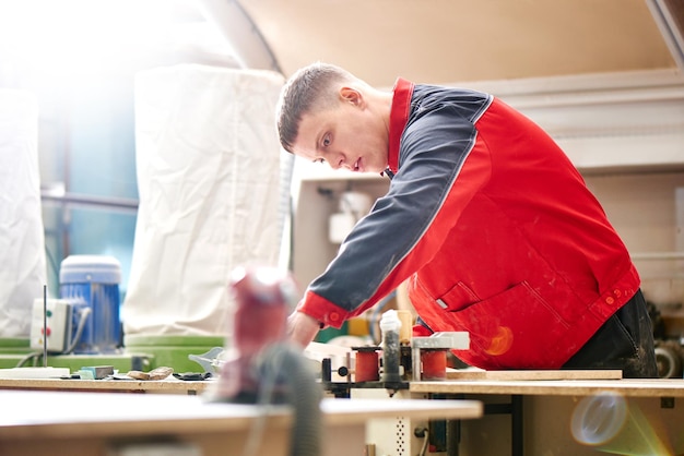 Process of production and manufacture of wooden furniture in furniture factory Worker carpenter man in overalls processes wood on special equipment