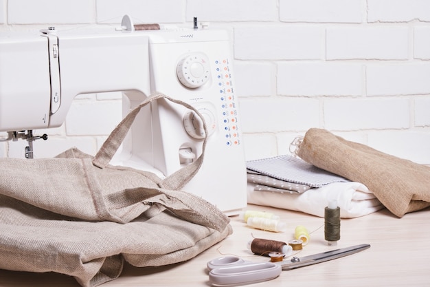 The process of sewing eco bags, thread, scissors and a sewing machine on the background of a white brick wall copy space