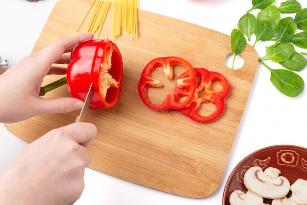 The process of slicing bell peppers. Mushrooms, spinach leaves, spaghetti on a white background.