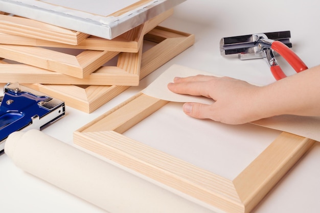 The process of stretching the canvas on a stretcher in the framework shop. The artist's hand wraps the canvas around a wooden stretcher.