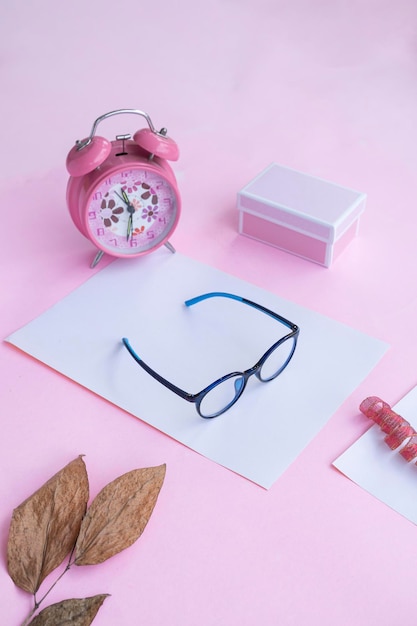 Product Presentation of Minimalist Concept Idea glasses gift box clock and dry leaves on pink paper background