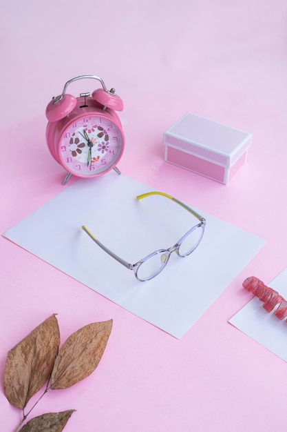 Product Presentation of Minimalist Concept Idea glasses gift box clock and dry leaves on pink paper background