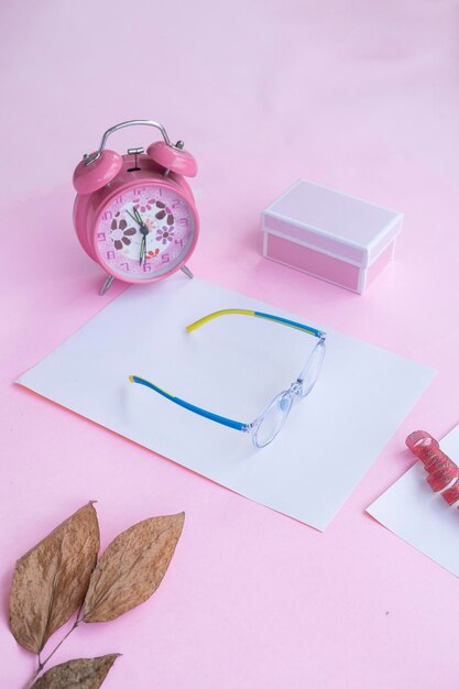 Product Presentation of Minimalist Concept Idea glasses gift box clock and dry leaves on pink paper background