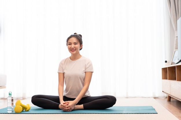 Productive activity concept a girl with a bun sitting on the rectangular green mat stretching her both legs parallel to the floor.