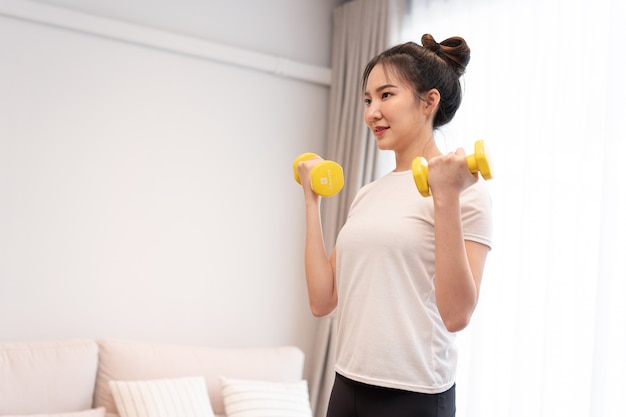 Productive activity concept a girl with a bun wearing a white t-shirt raising the yellow dumbbell with her right hand in her living space.