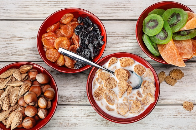 Products for healthy breakfast. Wooden bowls with nuts, dried fruits. Cereal flakes with milk.