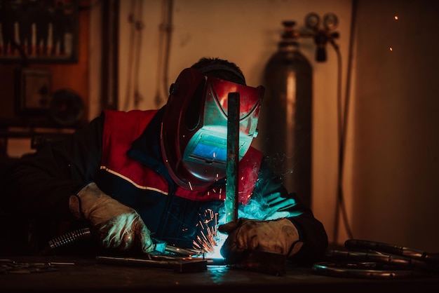 Profesional welder in protective uniform and mask welding metal pipe on the industrial table with ot