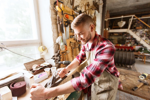 profession, carpentry, woodwork and people concept - carpenter working with plane and wood plank at workshop