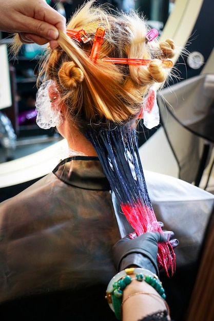 Photo a profession hairdresser is painting red color on hair tip and some other dark color at root