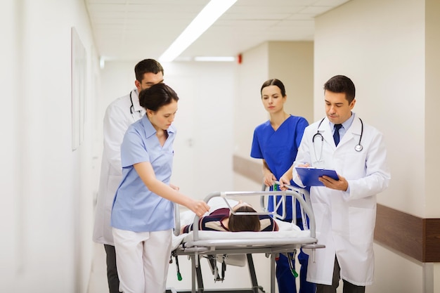 profession, people, health care, reanimation and medicine concept - group of medics or doctors carrying unconscious woman patient on hospital gurney to emergency