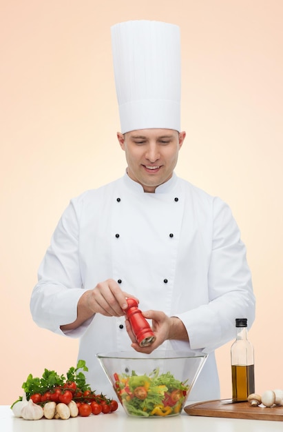 profession, vegetarian, food and people concept - happy male chef cooking and seasoning vegetable salad over beige background