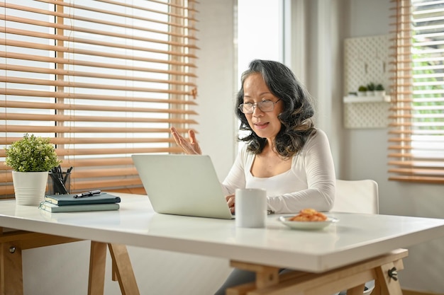 Professional 60s Asianaged businesswoman having an online meeting with her team