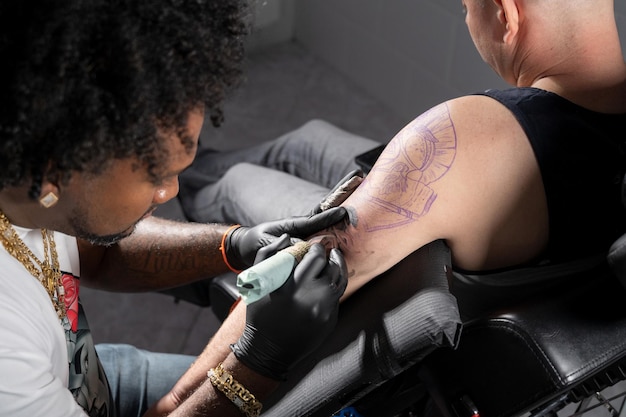 Professional African American tattoo artist makes a tattoo on client arm