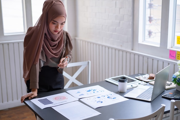 Professional arab businesswoman brown hijab standing and checking in financial investment project graph chart report.