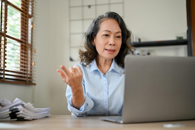 Professional Asian aged businesswoman looking at the laptop screen working at her desk