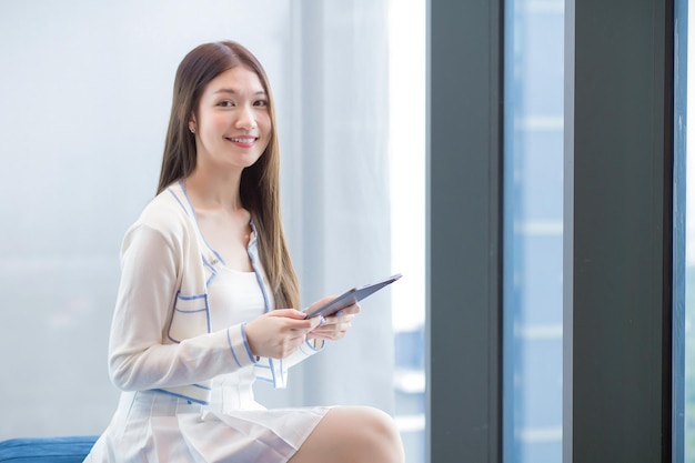 Professional Asian business woman with long hair in white shirt holds tablet in workplace office