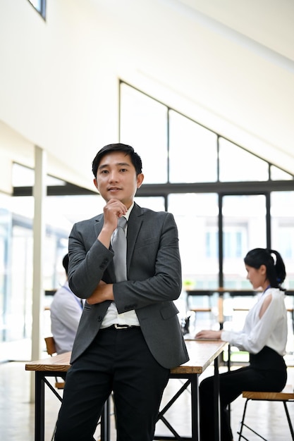 A professional Asian businessman in a formal business suit stands in the office room