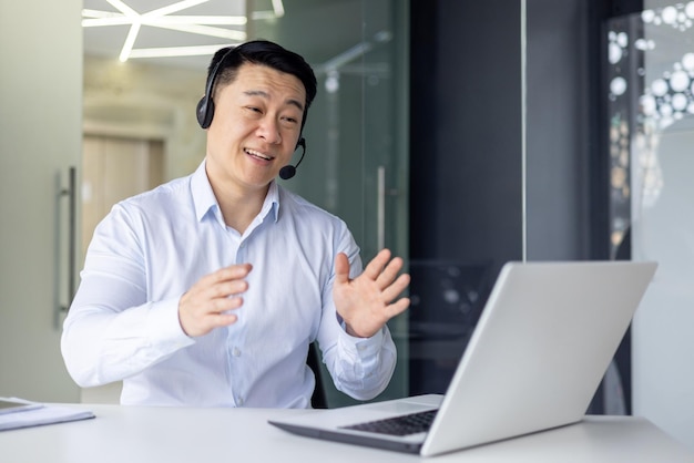 Professional asian businessman in a headset engaged in a video call explaining with hand gestures in