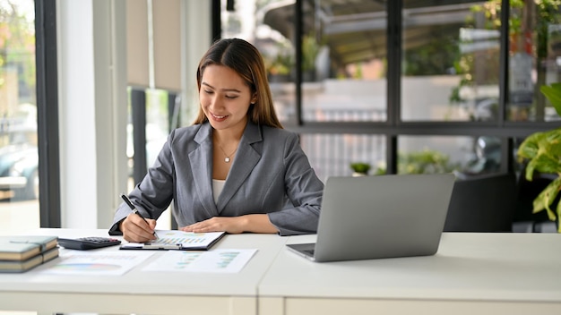 Professional Asian businesswoman examining and analyzing sales data on reports at her desk