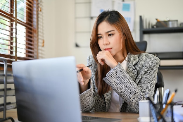 Professional Asian businesswoman pensively thinking analyzing the data on laptop screen