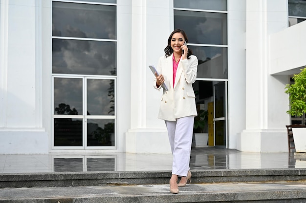 Professional Asian female boss walking out of the building while talking on the phone