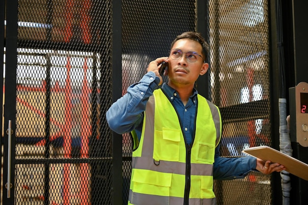 Professional Asian male warehouse supervisor talking on the phone while working in warehouse