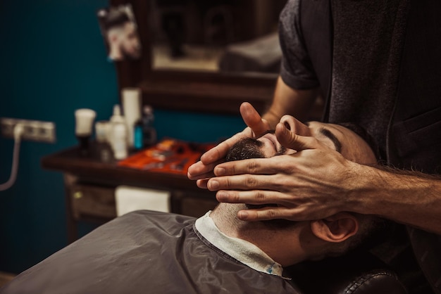 A professional barber cuts his beard to a young hipster man