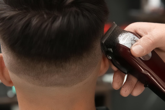 Professional barber making stylish haircut in salon closeup